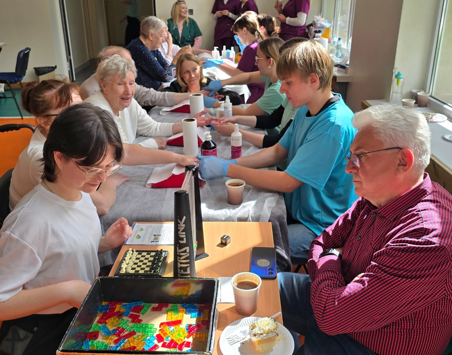 Widok na seniorów grających w planszówki oraz zażywających zabiegi pielęgnacyjne dłoni.