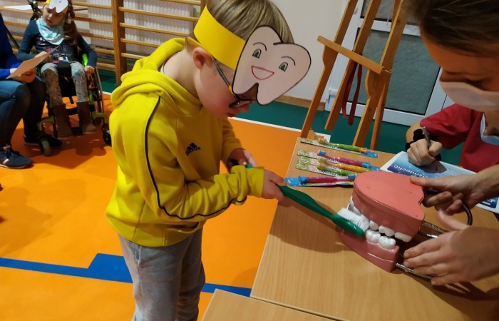 Dzieci na hali sportowej uczą się dbania o zęby i jamę ustną.