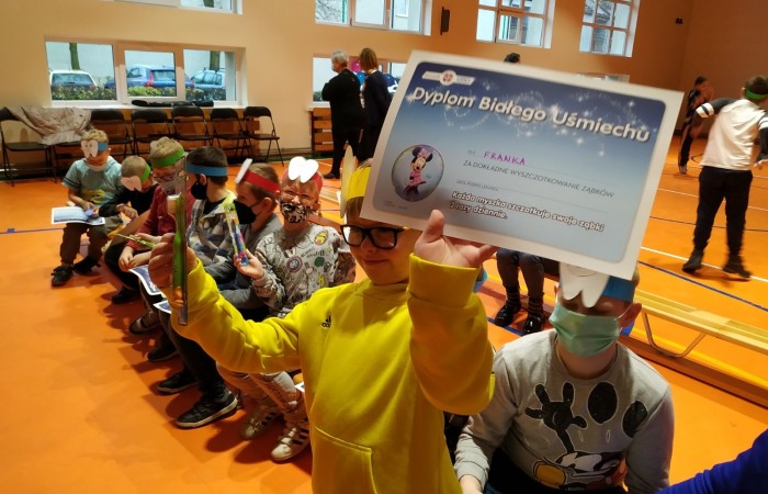 Dzieci na hali sportowej uczą się dbania o zęby i jamę ustną.