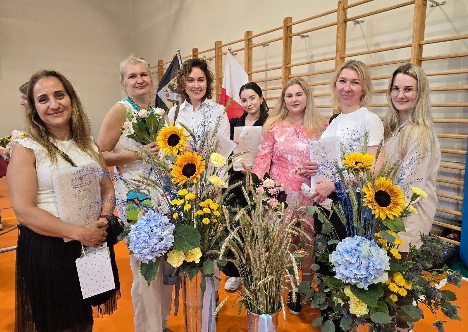 Wspólne zdjęcie uczniów i nauczycieli z kwiatami.