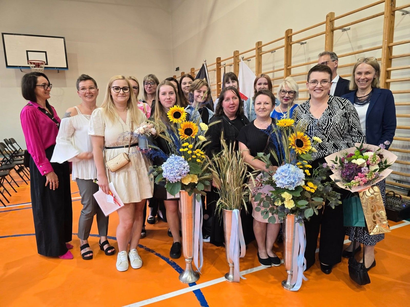 Wspólne zdjęcie uczniów i nauczycieli z kwiatami.