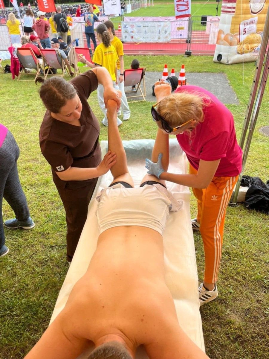 Uczennice wykonujące masaż stup i łydek uczestnika na stole.