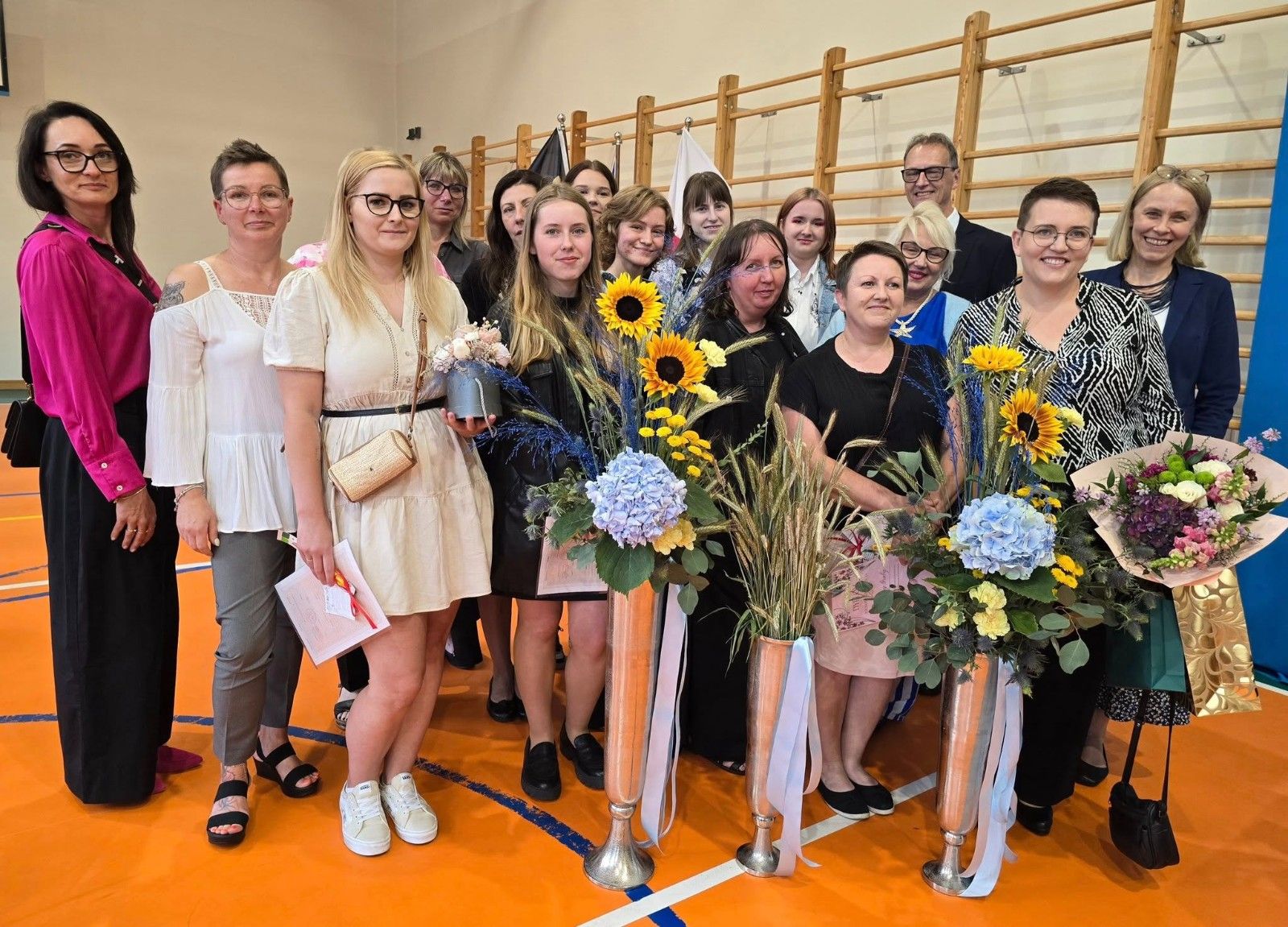 Wspólne zdjęcie uczniów i nauczycieli z kwiatami.