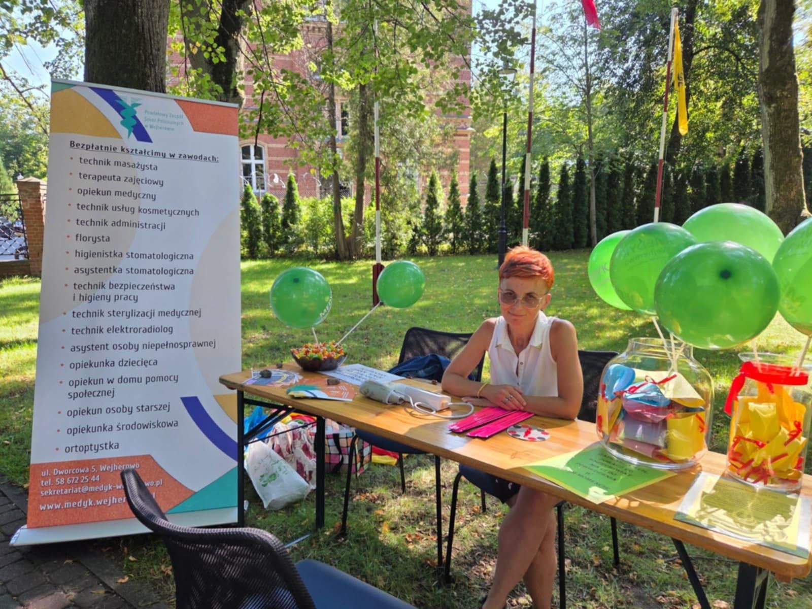 Zdjęcie uczestnika dni otwartych podczas słonecznej pogody przy stole z balonami.